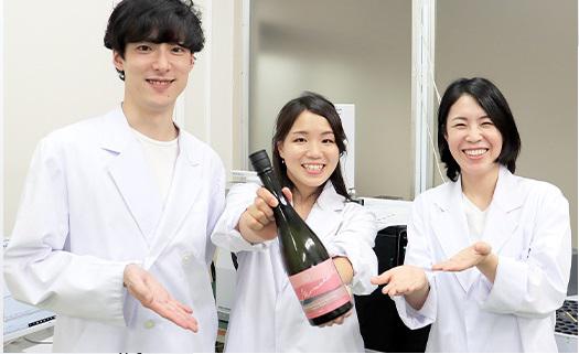 笑顔で日本酒の瓶を差し出す白衣の社員たち